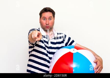 portrait of a serious middle age guy holding beach ball and showing to you gesture on white studio wall. Stock Photo