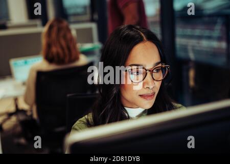 Portrait of mixed race woman working on business report typing on desktop sitting in office block Stock Photo
