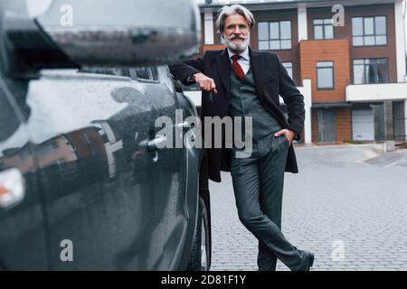 Fashionable senior man with gray hair and beard leaning on his car and holding keys Stock Photo