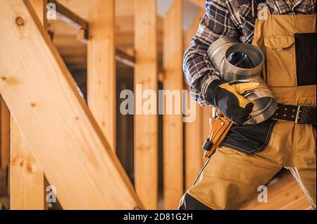 HVAC Technologies Theme. Air Ventilation Technician with Piece of Metal Air Shaft in His Hands Staying In Wooden Home Attic. Stock Photo
