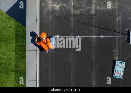 Caucasian Technician Wearing Orange Uniform and Hard Hat Installing Lightning Protection System Rod on Top of Commercial Building. Protect Structure F Stock Photo