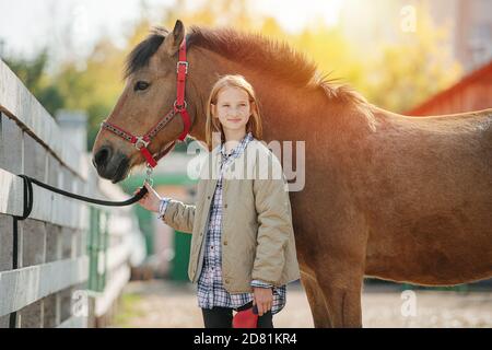 Proud satisfied little ginger girl posing with her horse. Smiling Stock Photo