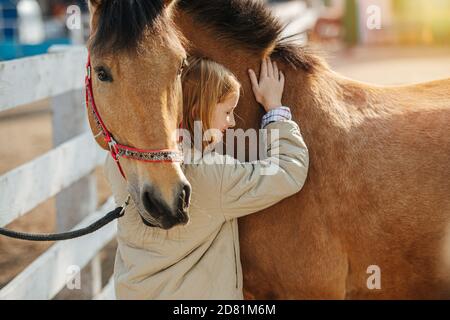 Friendship of a little ginger girl and her horse. Touching and leaning Stock Photo