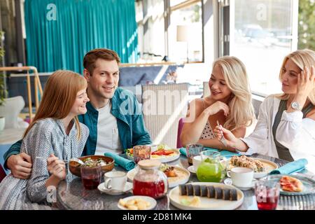 happy young caucasian friends gathering in cafe, sitting at table, chatting, talking.they are spending funny time, students or best friends meeting Stock Photo