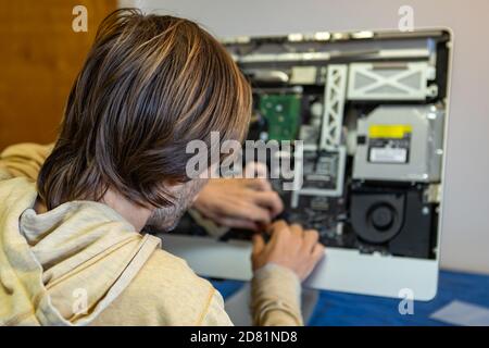 Rear view of young male engineer in a hoodie busy, and focused in fixing and assembling parts of a fancy desktop computer in modern office Stock Photo
