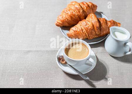 Croissants and cup of coffee in the morning light, sunlight shadow, on a linen fabric. Morning breakfast concept. Stock Photo