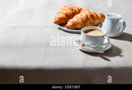 Croissants and cup of coffee in the morning light, sunlight shadow, on a linen fabric. Morning breakfast concept. Stock Photo