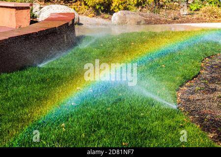 Lawn sprinklers and sun create a rainbow of color Stock Photo