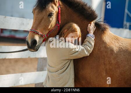Immersed ginger girl with lovely freckles petting and hugging her horse. Stock Photo