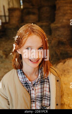Funny ginger girl with wood shavings on her hair inside big barn Stock Photo