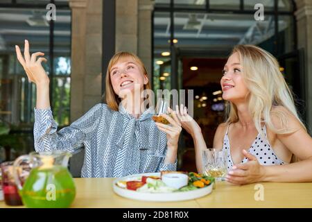 two positive caucasian women enjoy spending time together in restaurant, blonde females have talk and drink beverages, enjoy meal. they haven't seen each other for a long time Stock Photo