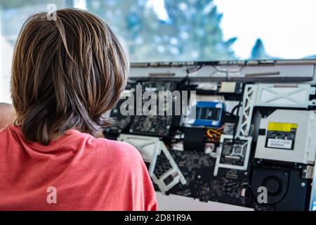 Rear view of male computer engineer diagnosing issue repairing and fixing the same with broken computer in office using tools  Stock Photo