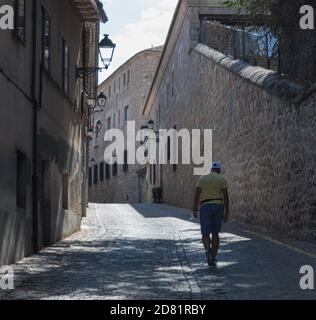 young man in shorts and sun hat climbing a hill in the streets of a Romanesque city on a sunny day Stock Photo