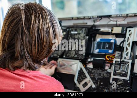 Rear view of young male technician with long hair fixing and resolving issue with broken fancy desktop computer in office using tools  Stock Photo