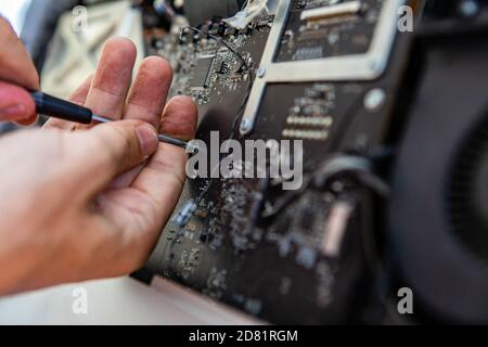 Selective focus of male technician hands holding screw driver tool to unscrew bolts in fancy desktop computer while repairing Stock Photo