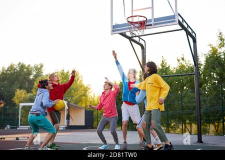 group of young male teenagers in colourful hoodies playing basketball outdoors in the street Stock Photo