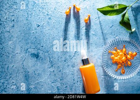 Messy composition and hard light with copy space. Vitamin C concentrate capsules, a facial serum in a dropper orange bottle and a branch with orange l Stock Photo