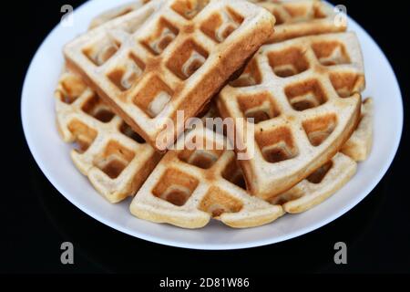 Belgian waffles in white plate on black glass table. Healthy breakfast, pieces of freshly baked classic wafer Stock Photo