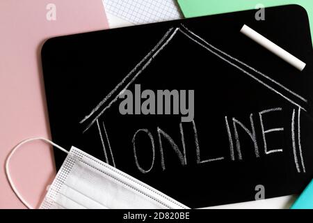 Online handwritten with chalk on blackboard, notebook and medical mask on the table. Top view Stock Photo