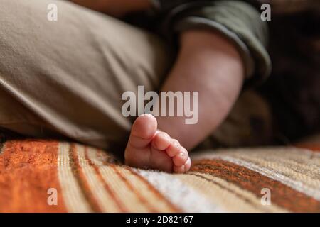 Selective focus of tiny little feet and fingers of newborn infant baby boy relaxing on fathers lap while sitting on couch at home Stock Photo