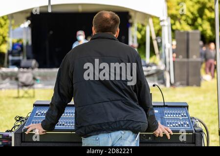 Rear view of young man wearing jacket standing behind electronic sound equalizer while staring at stage arrangement in cultural fiesta Stock Photo
