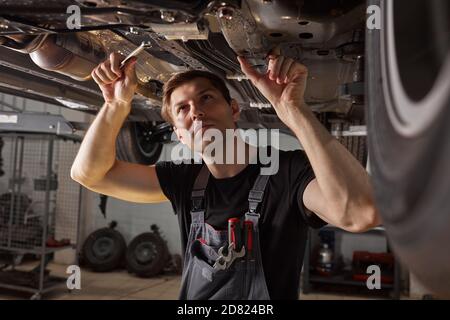 handsome caucasian male repairing bottom of car, check and examine all details. hardworking man in uniform at work Stock Photo