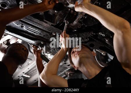 two friendly professional auto mechanic during work, they are successfully repairing car, solve problems together Stock Photo