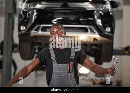 portrait of positive afro american auto mechanic in uniform posing after work, he is keen on repairing cars, automobiles. Stock Photo