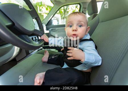 Portrait of excited and curious infant baby boy in formal clothing sitting on driver's seat holding steering wheel and looking outside Stock Photo