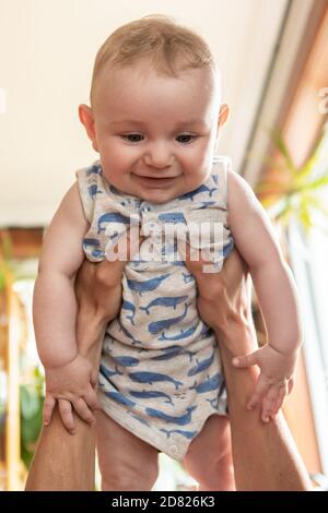 Selective focus of young father hands holding smiling infant baby child in air and playing while lying on couch at home  Stock Photo