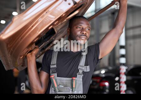 confident auto mechanic holding seperate part of the car, going to repair it at work place, hold it above head Stock Photo