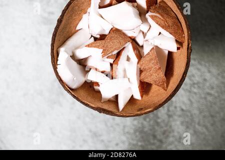 A bowl of coconut pieces on concrete background. Coconut ingredient on plate. Vegan organic snack in zero waste coconut bowl Stock Photo