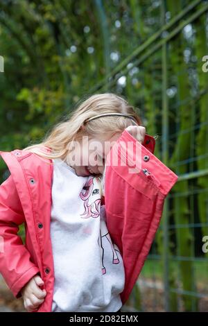 Cute blond little girl covers her face with her hand for the photo, private life and children concept Stock Photo