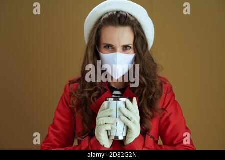 Life during coronavirus pandemic. Portrait of stylish woman in red coat with mug on brown background. Stock Photo