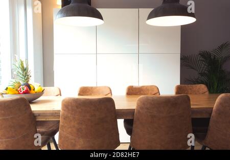 Modern wooden table with set of stylish chairs, houseplant, fruit in retro dining room, new interior design house Stock Photo