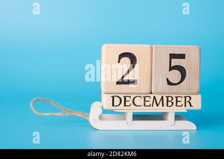 Waiting for the day concept. Close up photo of wooden calendar showing the 25th of december standing on sledges isolated over blue background Stock Photo