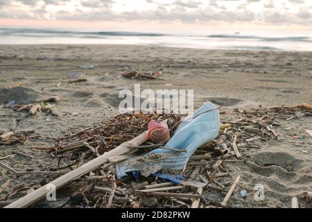 Dirty used surgical face mask discarded on dirty sea coast ecosystem,covid19 pandemic disease pollution effects Stock Photo