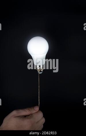 Hand holding a light bulb. Power saving light bulb is shinning and floating in darkness like a balloon. Conceptual minimalist background. Stock Photo