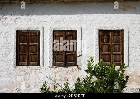 three windows of wooden on the whitewashed wall of a greek house Stock Photo