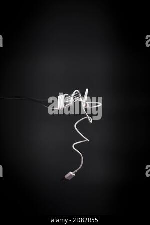 Charging mobile phone cable wrapped around fork like spaghetti. Dark grey background with fork and power cable in front. Conceptual photograph. Stock Photo