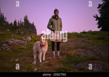 Dog and male in puffy coat watching the sunset with purple sky Stock Photo