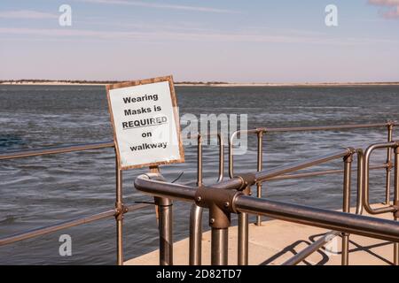 wearing masks is required on walkway sign behind a sheet of clear plastic at the Barnegat lighthouse jetty in New Jersey with view of the water behind Stock Photo
