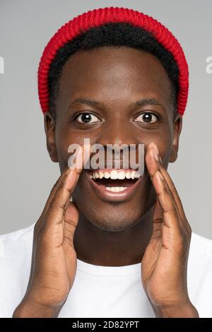 Surprised Black man in white t-shirt hold hands near mouth, whispering telling something confidential share secret hidden information about sale and b Stock Photo