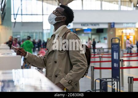 African American man stands at check-in counters at the airport terminal, giving passport to an officer. Flight rules during a Covid-19 pandemic only Stock Photo
