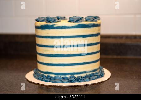 A white and blue round frosted multilayered birthday cake. The tall cake has blue rosettes on the top. Stock Photo