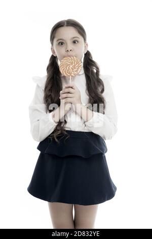 Sweets reward for study. Rewarding herself with sweets. Food addictions. Girl kid eat sweet lollipop. Girl pupil school uniform like sweets lollipop candy white background. Healthy nutrition diet. Stock Photo