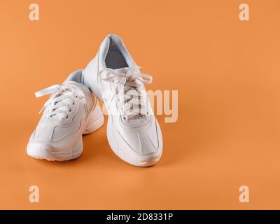 Pair of white tied laces sneakers over an orange background. New unisex chunky sole shoes for active lifestyle, fitness and sports. Copy space. Stock Photo
