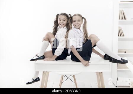 Rebellious spirit. School club. Little schoolgirls classmates friendly kids. Schoolgirls friends sit on desk. Best friends relaxing. Schoolgirls tidy hairstyle relaxing having rest. School uniform. Stock Photo