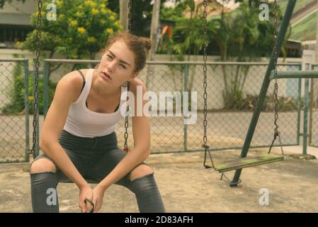 Young beautiful teenage girl sitting on the metal swing in old playground Stock Photo