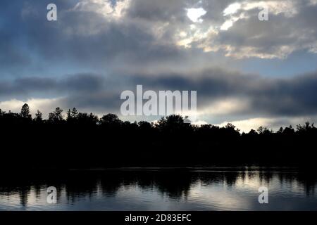 Treeline reflected in water - looking west across Dow's Lake with a wonderful late afternoon sun and interesting cloudscape. Ottawa, Ontario, Canada. Stock Photo